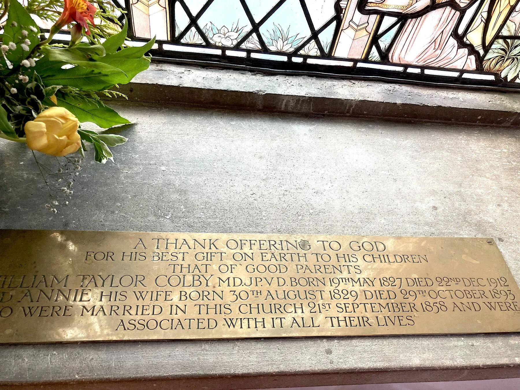 Brass plaque below the window, partly hidden by flowers