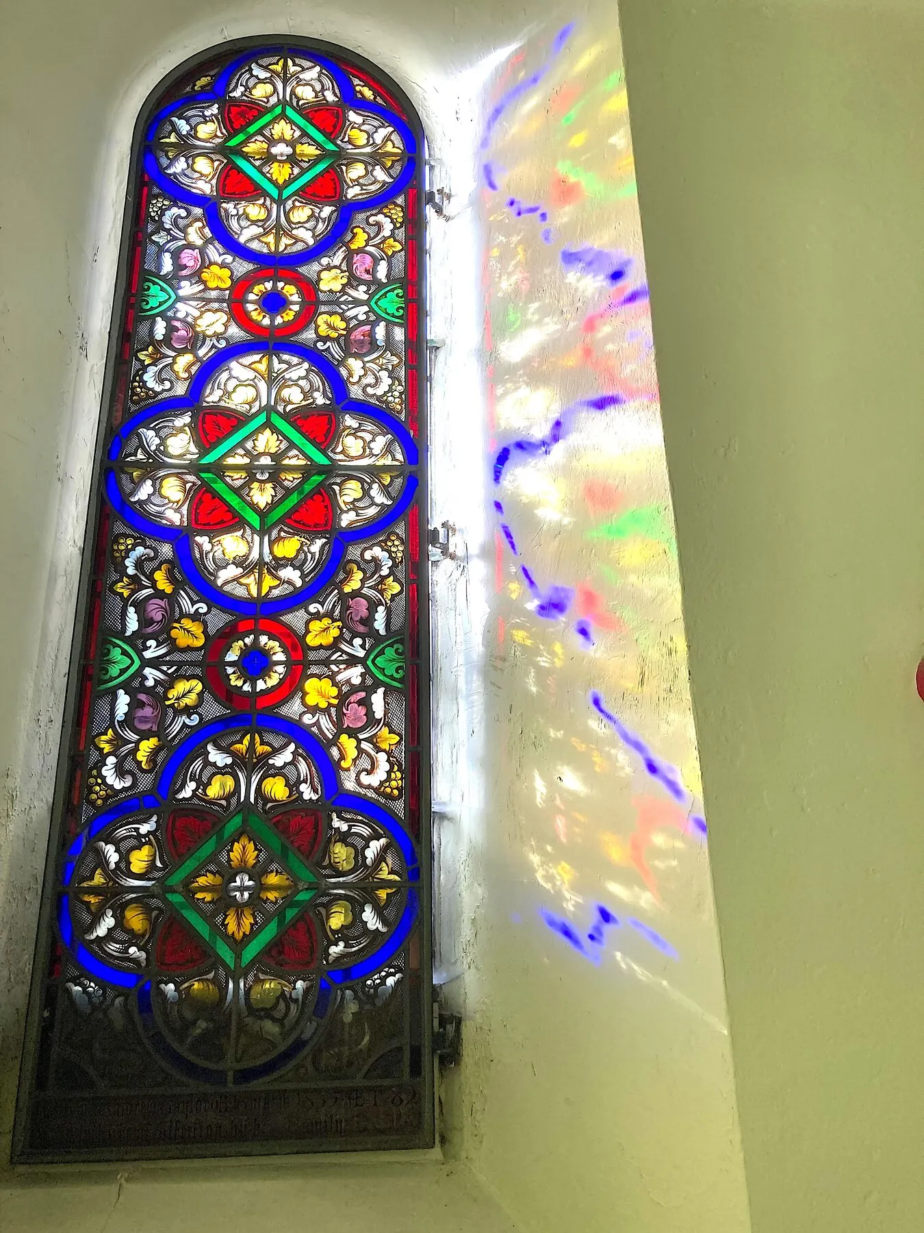Narrow lancet window with red, blue and gold glass, sunlight casting colours on the wall