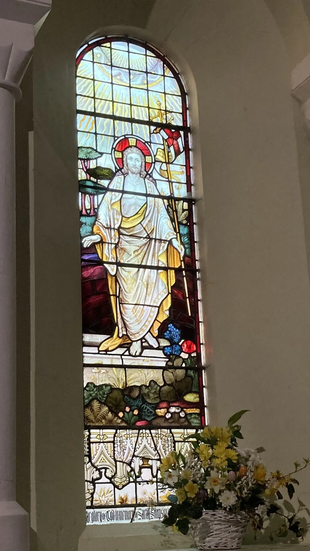 Arched stained glass window with a robed figure, between white stone columns