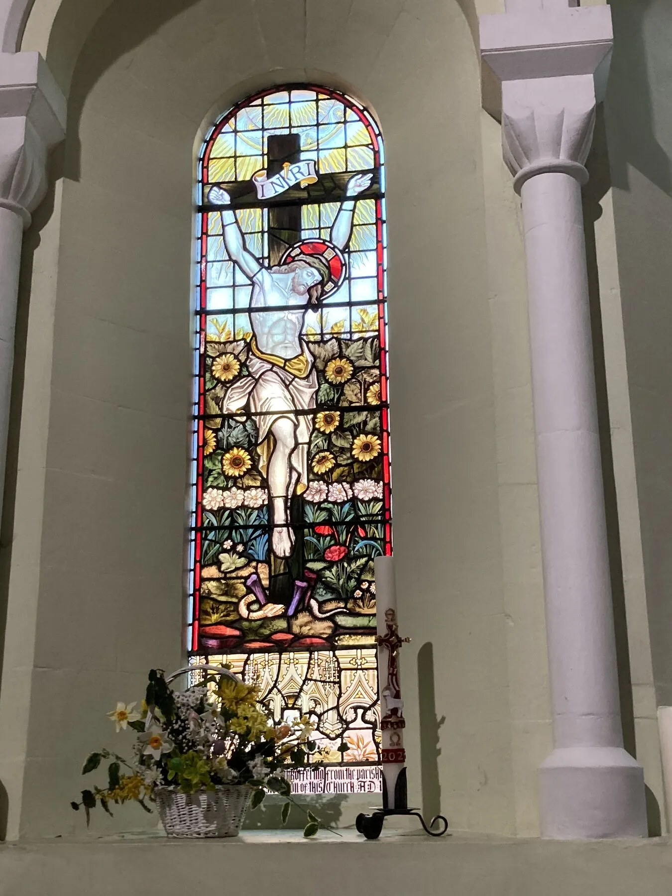 Arched stained glass window above flowers, between white stone columns
