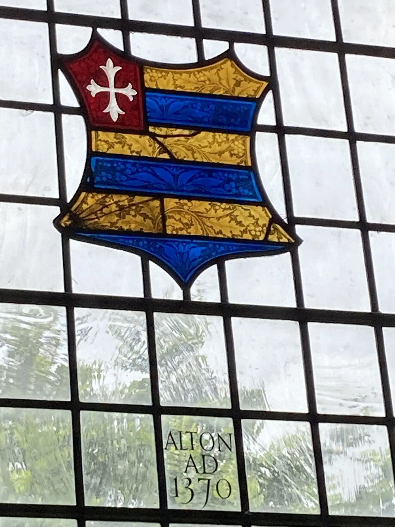 A heraldic shield with blue and gold bands and a red cross, set in plain glass