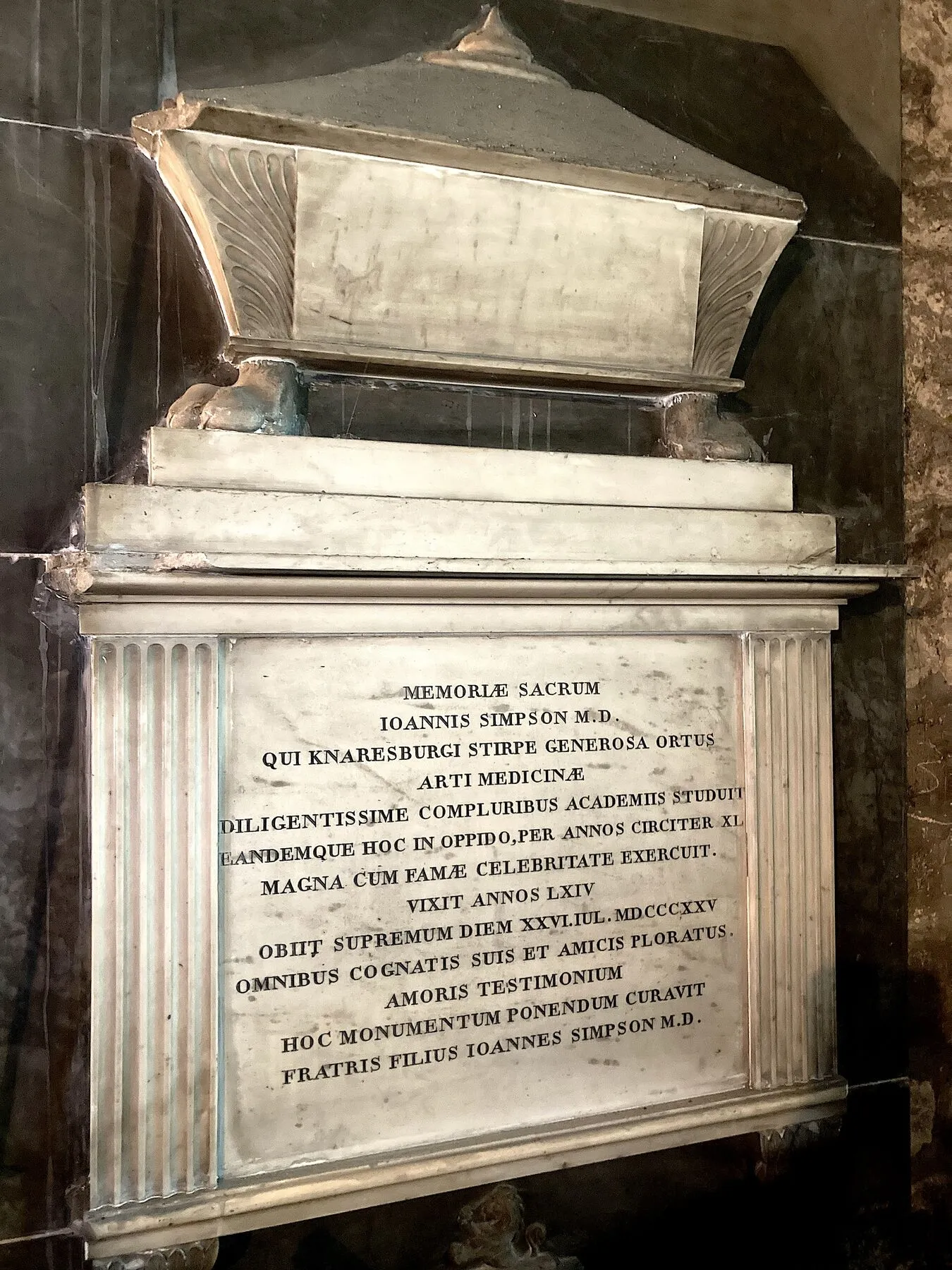 A white marble tablet carved in the shape of a sarcophagus