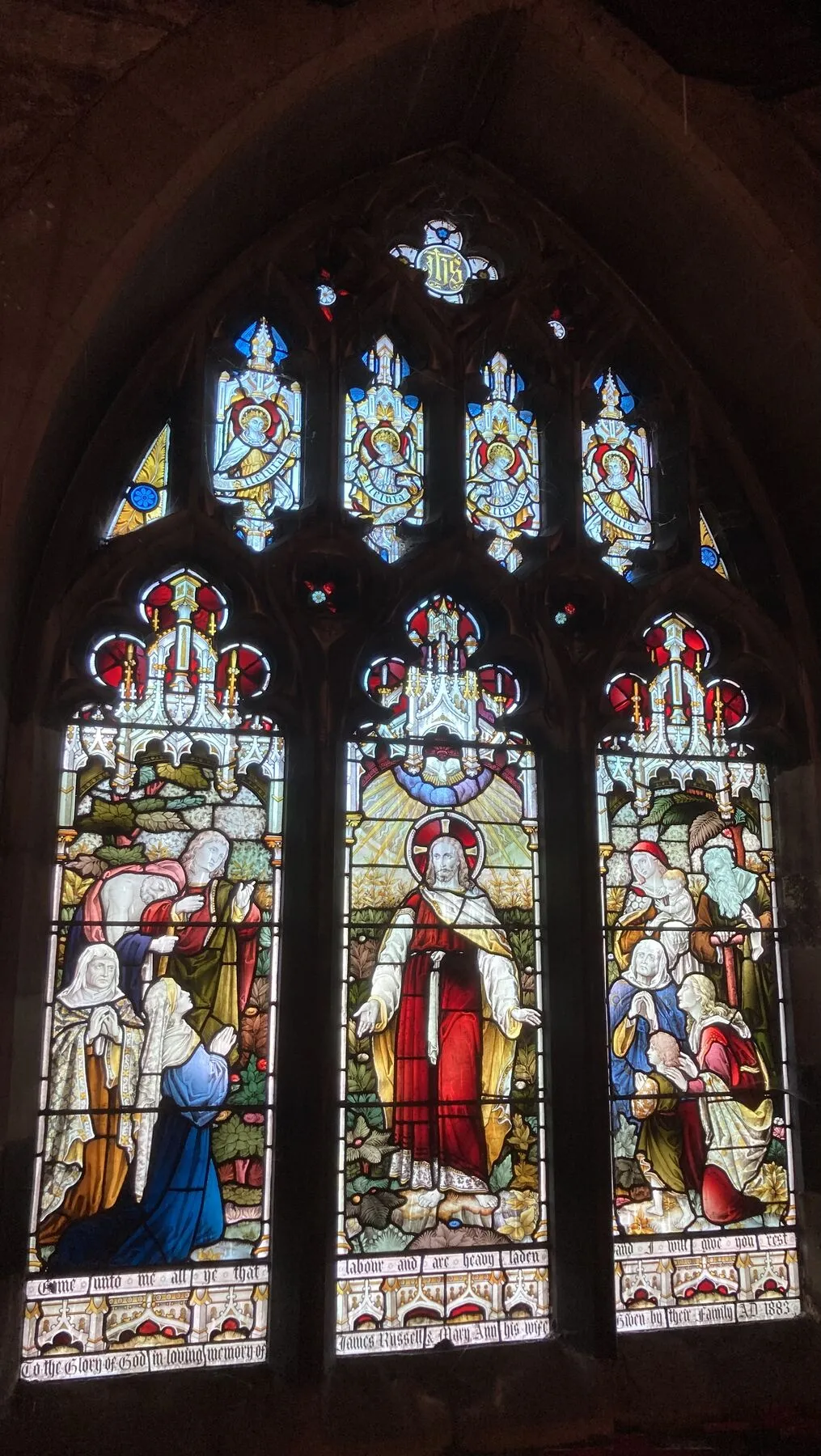 A large three-light window of richly coloured figures under canopies